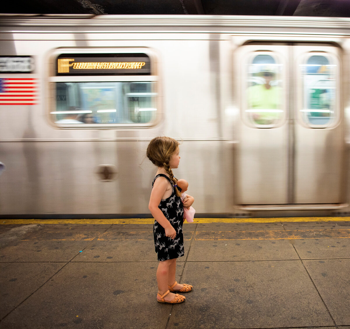 Girl with doll standing in front of a subway