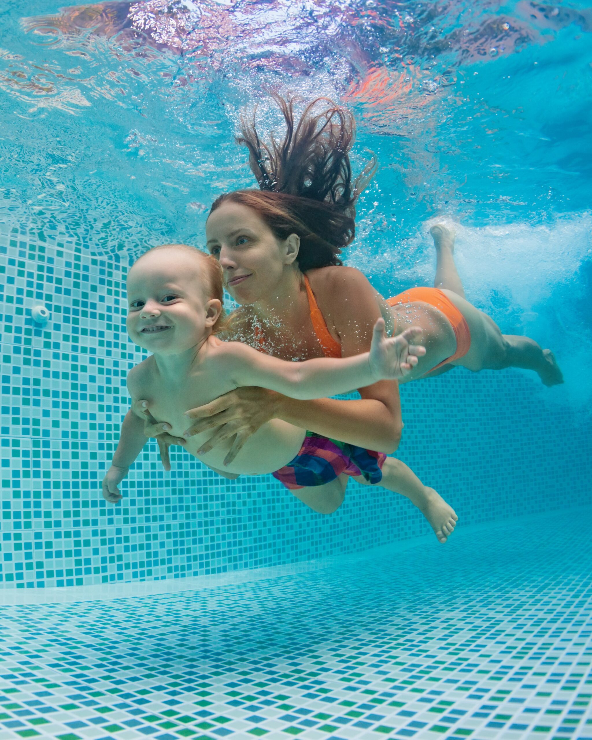 Mother, father with baby swimming, diving underwater in pool