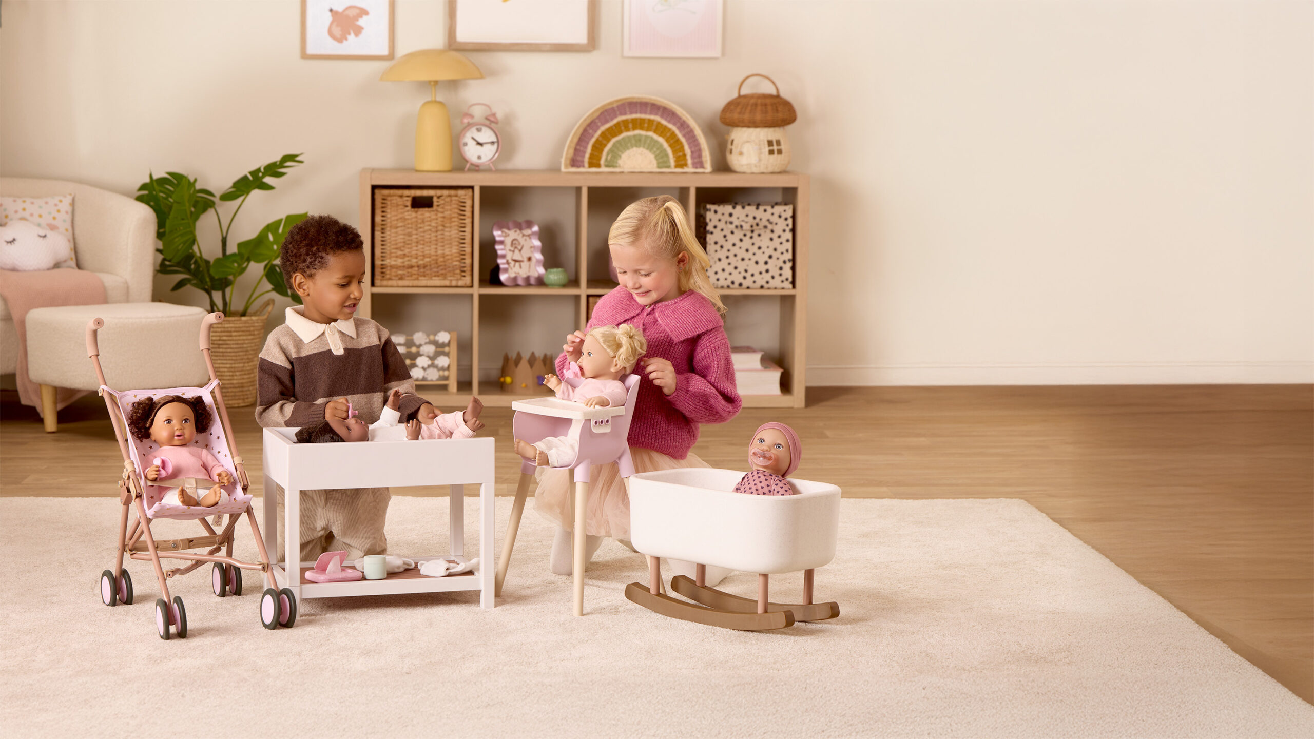 Two children playing with baby dolls, using a changing table, high chair, stroller, and rocking cradle in a cozy, decorated living room